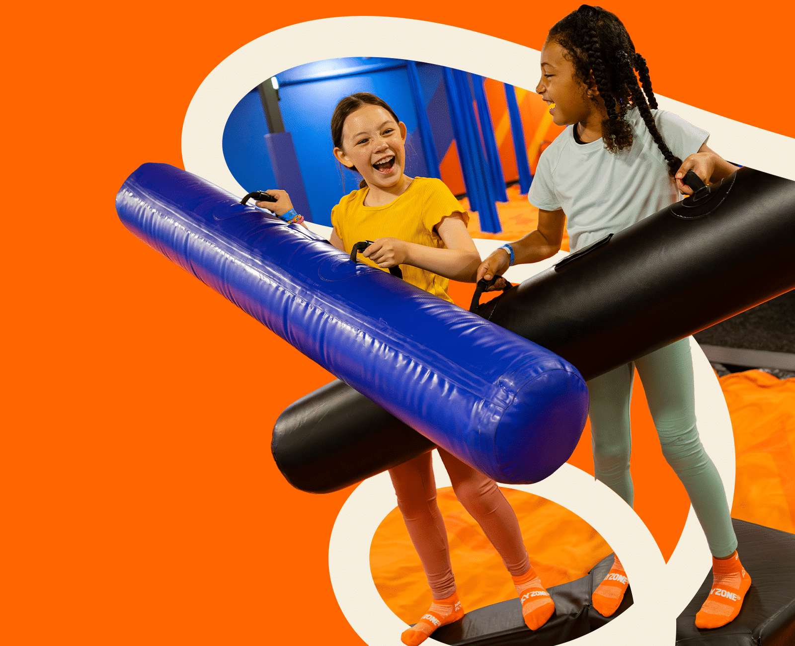 Two kids laughing while playing joust with padded beams on an elevated platform at a trampoline park.